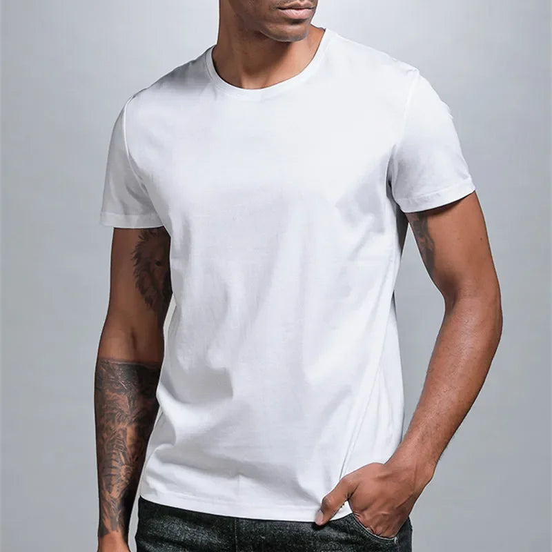 A fit man with tattoos on his right arm is wearing a pur cotton, white t-shirt and looking to his left