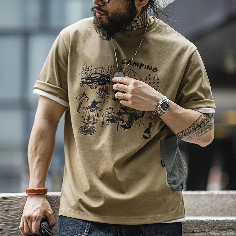 A bearded man wearing a graphic t-shirt in brown color is leaning against a stone wall and looking to his right